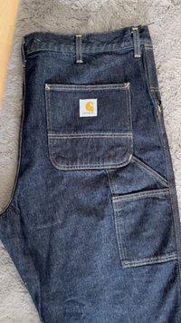 Pantalones de mezclilla azul oscuro con un corte estándar, costuras visibles y múltiples bolsillos, incluido un gran bolsillo trasero con un parche de logo.