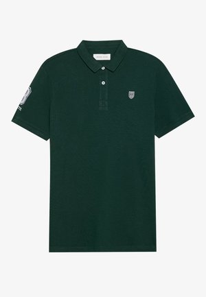 Temno zelena polo majica iz teksturiranega materiala, s klasičnim ovratnikom, dvema gumboma in izvezenimi logotipi na prsih in rokavu.