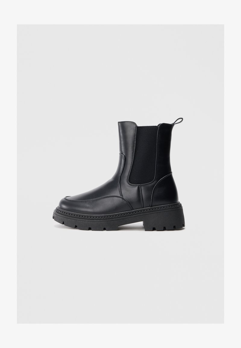 Botas Chelsea pretas feitas de couro suave, com painéis elásticos nas laterais, sola grossa e robusta, e uma pega na parte de trás para facilitar o calçar.