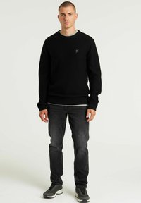 Maglione nero a maglia con un motivo testurizzato, scollo rotondo e patch del logo. Abbinato a jeans scuri e sneakers grigie.