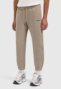 Beige joggerpants met een trekkoord in de taille, manchetten bij de enkels en een klein zwart logo op de dij, gemaakt van zachte, lichte stof.