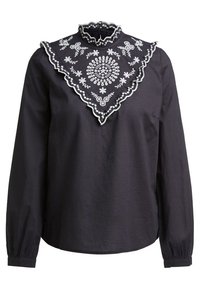 Sort langærmet bluse med høj krave, der har en dekorativ hvid broderet bærestykke med blomstermønstre og flæser.