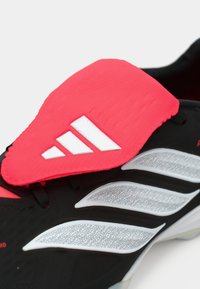 Μαύρο αθλητικό παπούτσι με υφή, διαθέτοντας έντονο ροζ ελαστικό επικάλυμμα και τρεις λευκές ρίγες στο επάνω μέρος.