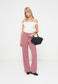 Top branco de ombro a nu com bordas em babados, calças largas listradas em vermelho e branco, bolsa preta, sapatos planos pretos, fundo simples.