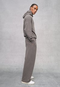 Grauer Baumwollhoodie mit Kängurutasche und Kordelzug. Kombiniert mit passender, weiter Sweatpants. Glatte Textur, lockere Passform, minimale Details.