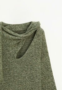 Zelený pletený top s vykrojeným výstřihem a volným střihem. Textura je měkká s kombinací tmavších a světlejších zelených vláken.