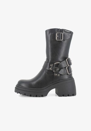 Botines negros con suela de plataforma gruesa, que presentan una textura similar al cuero suave, dos correas ajustables y un detalle de hebilla lateral.