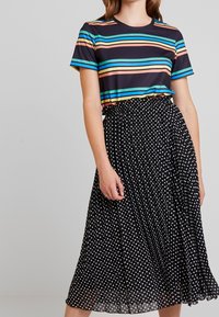 Camiseta a rayas en azul marino, naranja y turquesa; combinada con una falda negra con pliegues que presenta lunares blancos. Conjunto casual con cintura elástica.