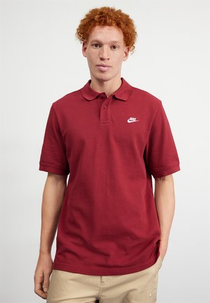 Red polo shirt made of cotton, featuring a collar, short sleeves, and a white Nike logo on the left chest. Casual design, solid color.