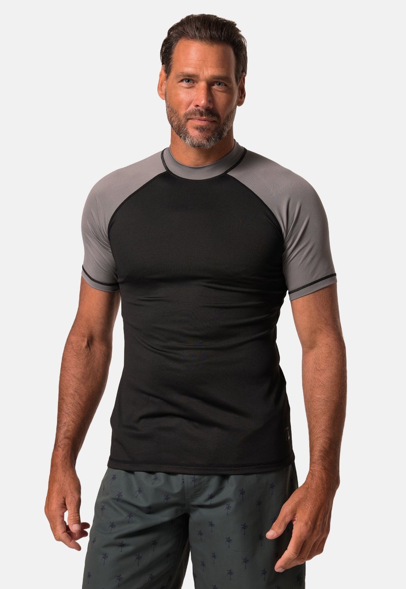 Rash guard s krátkým rukávem vyrobený z hladké černé tkaniny s šedými raglánovými rukávy. Má kulatý výstřih a těsný střih, ideální pro aktivní nošení.