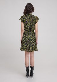 Vestido corto negro con patrón floral en amarillo y verde. Presenta mangas cortas, dobladillo acampanado y una cintura con lazo. Se lleva con botas de tacón negras.