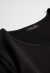 Top negro de tela con escote redondo y textura suave. Cuenta con una etiqueta que dice "Ysabel Mora para Mujeres" cerca del escote. Diseño simple.