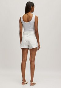 Witte tanktop gecombineerd met witte denim shorts met een rafelige zoom en achterzakken, gedragen met platte sandalen. Achteraanzicht getoond.