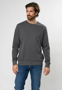 Grijze ronde hals sweatshirt met lange mouwen en ribgebreide boorden, voorzien van een klein donker logo op de borst, in combinatie met blauwe spijkerbroek.