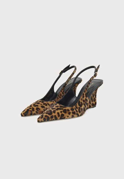 Paire de chaussures compensées slingback à bout pointu avec imprimé léopard marron et noir et brides noires à la cheville avec une boucle dorée, sur fond blanc.