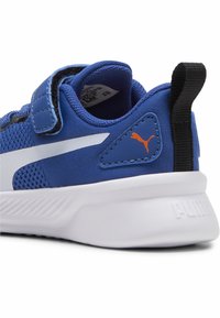 Zapatillas deportivas sintéticas azules con paneles de malla, acentos blancos, correa ajustable y una suela blanca texturizada. Presenta un pequeño logotipo naranja en el talón.
