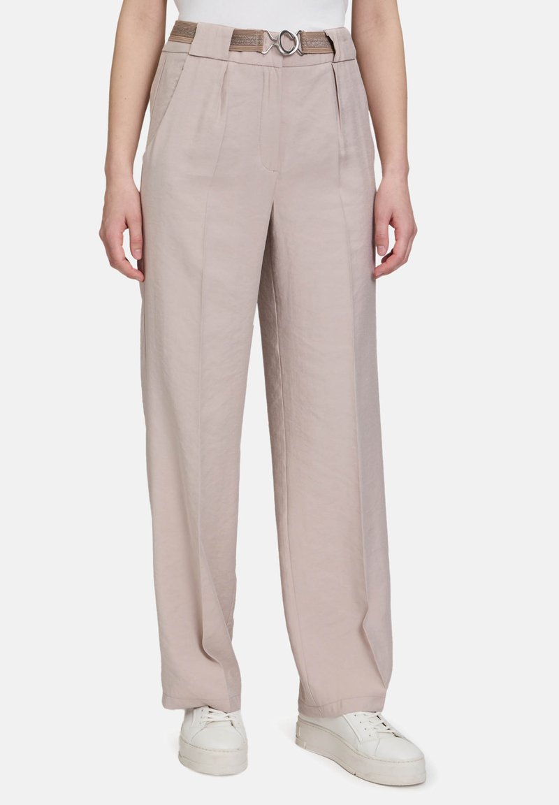 Pantalons larges beige clair en tissu léger, dotés de plis à l'avant et d'une ceinture texturée avec une boucle en argent circulaire.