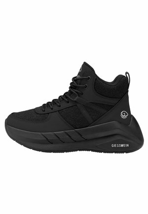 Zwarte hoge sneaker met dikke zool, textuurstofpanelen, veters aan de voorkant en Giesswein-logo op hiel en zool.