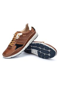 Zapatillas de cuero marrón con paneles perforados, acentos negros en contraste, cordones amarillos y una suela blanca moteada. Detalle de costura texturizada.