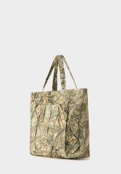 Τσάντα ώμου καμουφλάζ από υφασμάτινη υφή, με διπλές λαβές, μπροστινή τσέπη και ποικιλία γήινων χρωμάτων και σχεδίων.