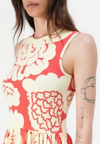 Floral-patterned dress featuring a ribbed texture in coral and cream colors. Fitted bodice with a flared skirt, sleeveless design.