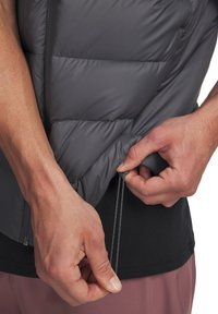 Gray puffer vest with a quilted design, lightweight fabric, and a side zipper being adjusted with hands. Textured surface, minimal detailing.