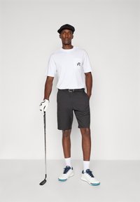 White t-shirt with pocket, black shorts, golfer's glove, and white athletic shoes with blue accents. Flat cap completes the look.
