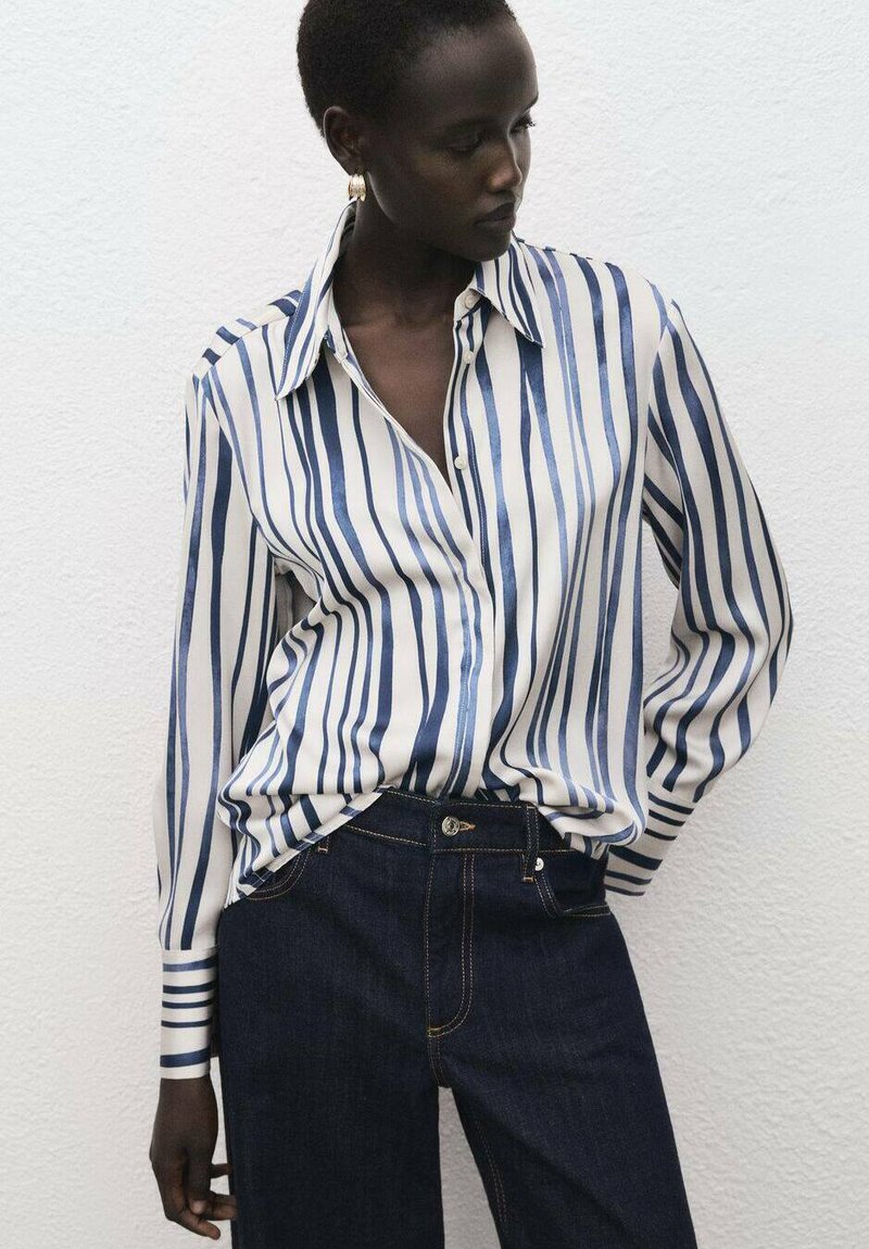 Modrá a biela pruhovaná košeľa na gombíky s golierom, s dlhými rukávmi a voľným strihom. Kombinovaná s tmavými rifľami.