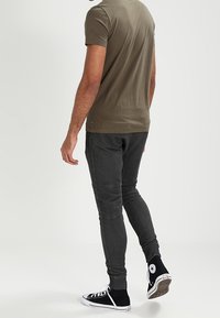 Olivegrön t-shirt med korta ärmar, kombinerad med slim fit mörka jeans och svarta högskaftade sneakers. Enkelt mönster, inga synliga motiv eller logotyper.