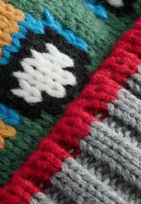 Nahaufnahme eines bunten gestrickten Stoffes mit Mustern aus grüner, blauer, schwarzer, weißer, gelber, roter und grauer Wolle.