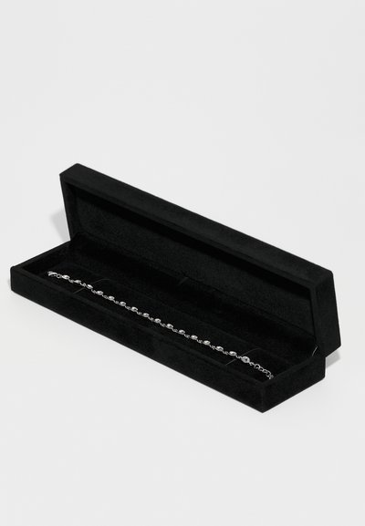 Silver bracelet displayed in a black velvet box, featuring circular links and a smooth metallic finish. The box has a rectangular shape.