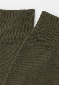 Olivgröna stickade strumpor med ribbad mudd och slät yta, som har ett enhetligt mönster och medel tjocklek.