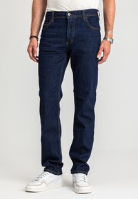 Ciemnoniebieskie dżinsy z denimu z kontrastującym pomarańczowym przeszyciem, klasycznym krojem z pięcioma kieszeniami i prostym fasonem, w połączeniu z białymi trampkami.