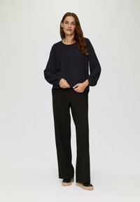 Navyblauwe blouse met lange mouwen, ronde hals, knoopdetail en geraffineerde mouwen, gecombineerd met zwarte wijde broek en platform schoenen.