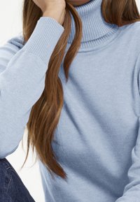 Hellblauer Rollkragenpullover mit geripptem Kragen und Bündchen, aus weichem Strickmaterial. Lange braune Haare sind teilweise sichtbar.