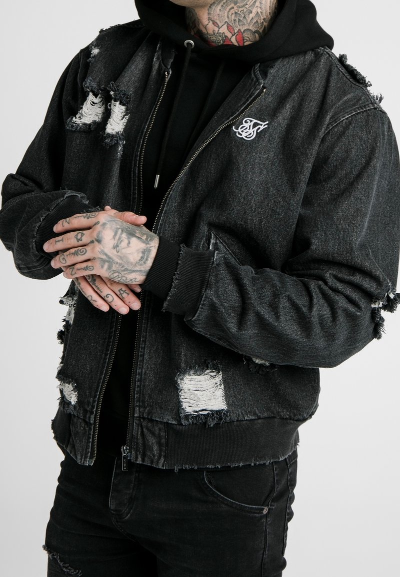 Czarna kurtka bomber z denimu z przetarciami, posiadająca postrzępione krawędzie i podarte łatki. Wyposażona w zamek błyskawiczny oraz haftowane logo.