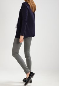 Marinblå cardigan med en avslappnad passform, grå slim fit-jeans och svarta lackskor. Cardiganen har en texturerad design och öppen front.