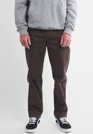 Pantalon marron droit en tissu mélangé coton, associé à un sweat-shirt gris et des baskets noires avec semelles et lacets blancs.