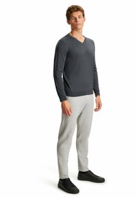 Dunkelgrauer V-Ausschnitt-Pullover mit langen Ärmeln, kombiniert mit hellgrauen Jogginghosen und schwarzen Sneakers. Der Pullover hat eine weiche Textur, die Jogginghosen verfügen über elastische Bündchen.