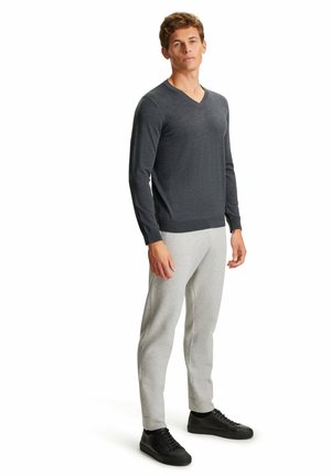Donkergrijze V-hals lange mouwen trui gecombineerd met lichtgrijze joggers en zwarte sneakers. De trui heeft een zachte textuur, de joggers hebben elastische boorden.