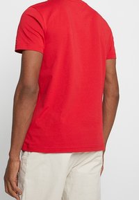 Camiseta de algodón roja con manga corta, color liso, cuello redondo y un ajuste relajado. La vista trasera muestra una textura suave sin adornos.