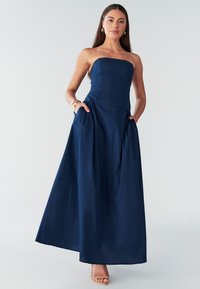 Maxi šaty bez ramienok v námorníckej modrej farbe s priliehavým živôtikom a nazbieranou sukňou, vybavené bočnými vreckami a hladkou, textúrovanou tkaninou.