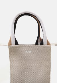 Borsa tote in tela beige con superficie testurizzata. Manici a contrasto in nero, bianco e marrone. Logo del marchio sul davanti.