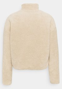 Beige, myk fleecejakke med høy krage og ingen synlige lukkinger. Har en teksturert, fluffy overflate og lange ermer.