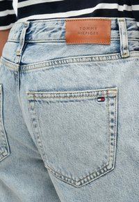 Svetlo modré denimové rifle s koženou nášivkou "TOMMY HILFIGER". Obsahujú štandardné vrecká a žlté šitie pozdĺž švov. Klasický strih.