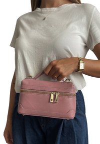 Różowa skórzana torebka o zwartej, prostokątnej formie, z górnym uchwytem, podwójnymi zamkami błyskawicznymi i złotymi akcentami metalowymi. Powierzchnia o fakturze.