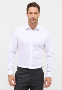 Witte lange mouwen shirt met een puntige kraag, voorzien van zwarte accenten op de manchetten en een knoopsluiting aan de voorkant. Glad, textuur stof.