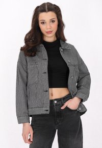 Svart och vit randig denimjacka med oversize-passform, framknappar och två bröstfickor, kombinerad med högmidjade svarta jeans.