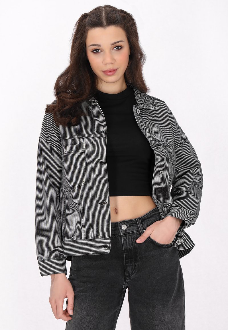 Svart och vit randig denimjacka med oversize-passform, framknappar och två bröstfickor, kombinerad med högmidjade svarta jeans.