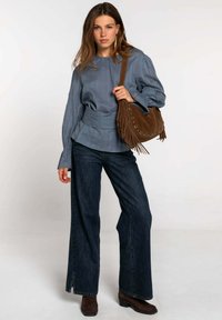 Blusa de rayas azul claro con mangas largas, combinada con pantalones vaqueros de pierna ancha en denim oscuro y bolso de ante marrón con flecos y herrajes circulares.